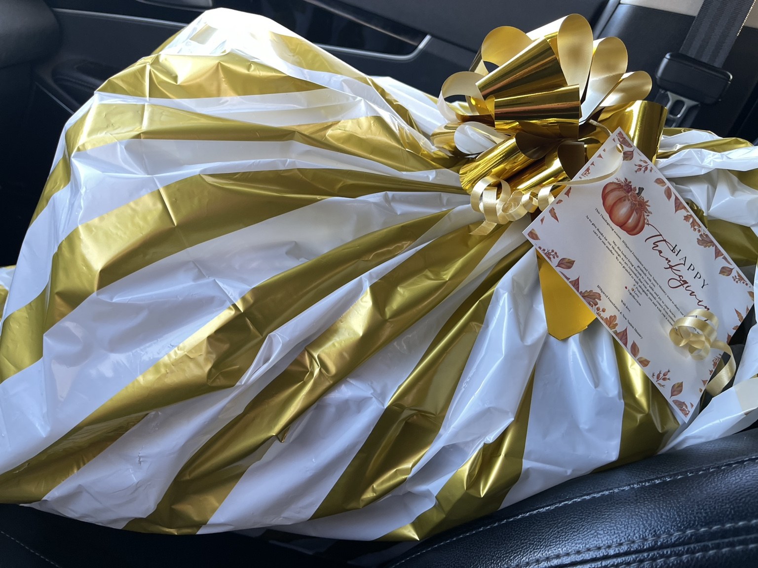 A holiday meal package wrapped in white and gold with a bow.